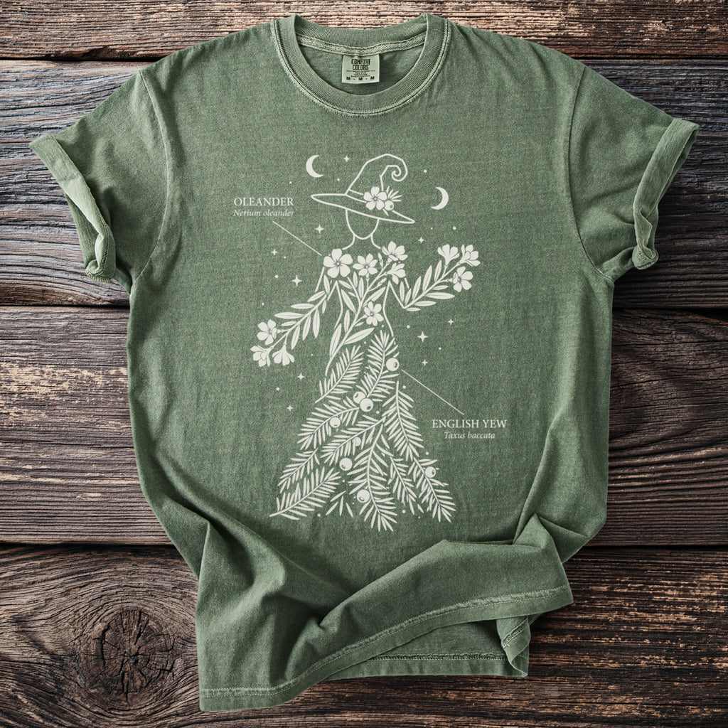 Green Comfort Colors t-shirt with white witch and floral design featuring "Oleander" and "English Yew" labels.
