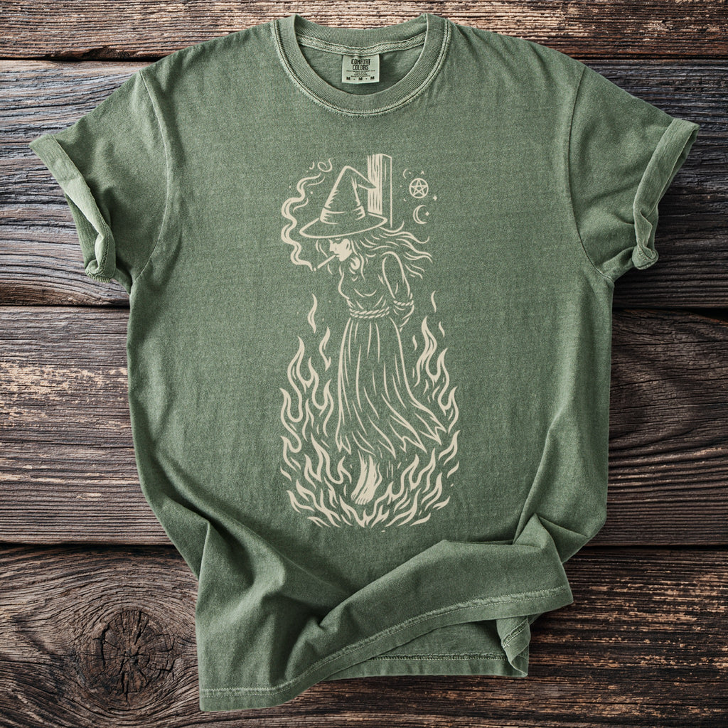 Green t-shirt with a cream graphic of a witch engulfed in flames.