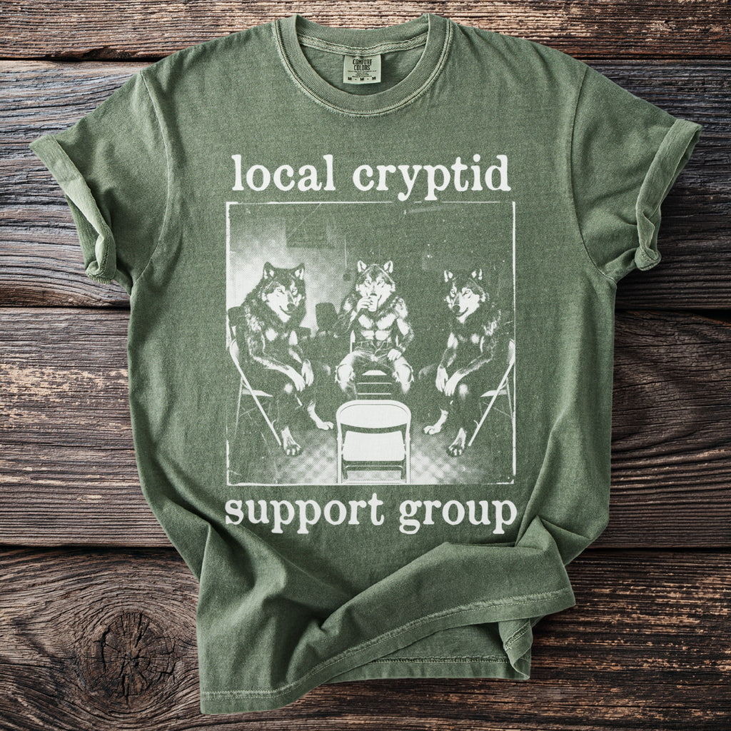 Green t-shirt with "local cryptid support group" text and image of three wolves.