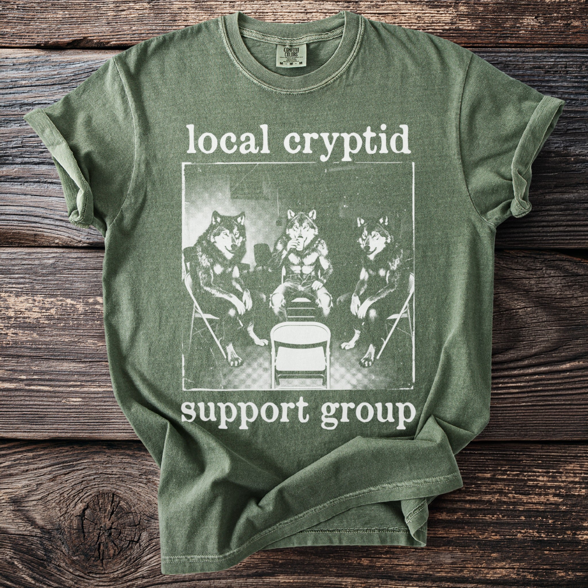 Green t-shirt with "local cryptid support group" text and image of three wolves.
