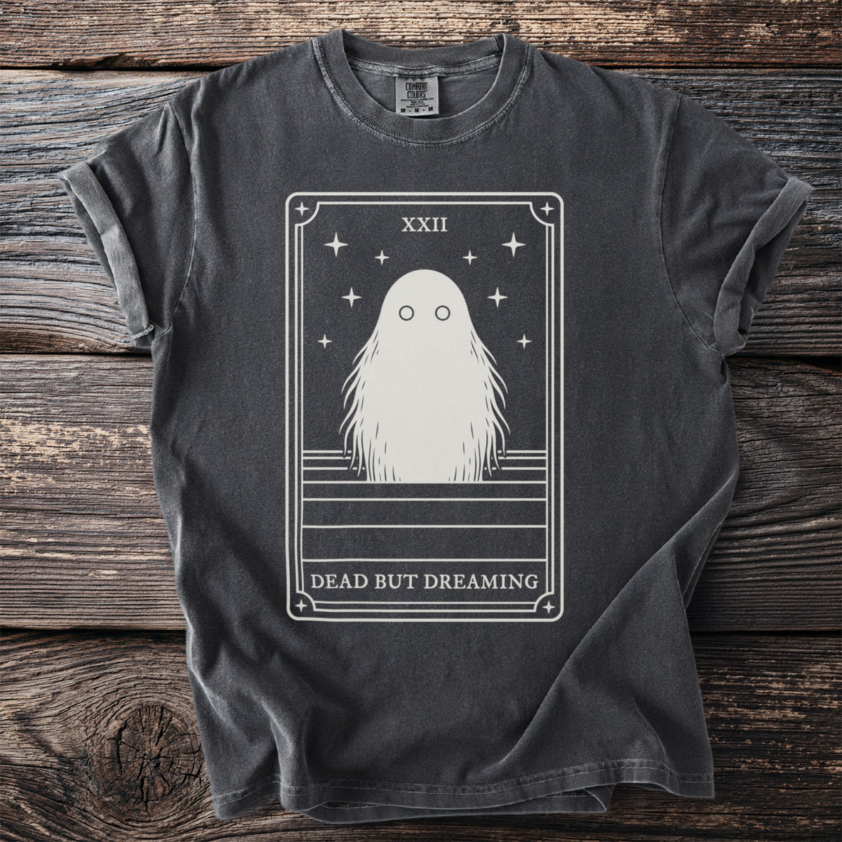 Dark t-shirt with a tarot card design featuring a ghost and "DEAD BUT DREAMING" text.