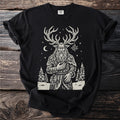 Black t-shirt with a cream folk-cut print: a bearded antlered god in a fur cloak stands among snowy pines, mistletoe hanging from his antlers.