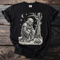 Black t-shirt with a cream folk-cut print: the Reaper crouches over a small fire in the snow, roasting chestnuts in a long pan.