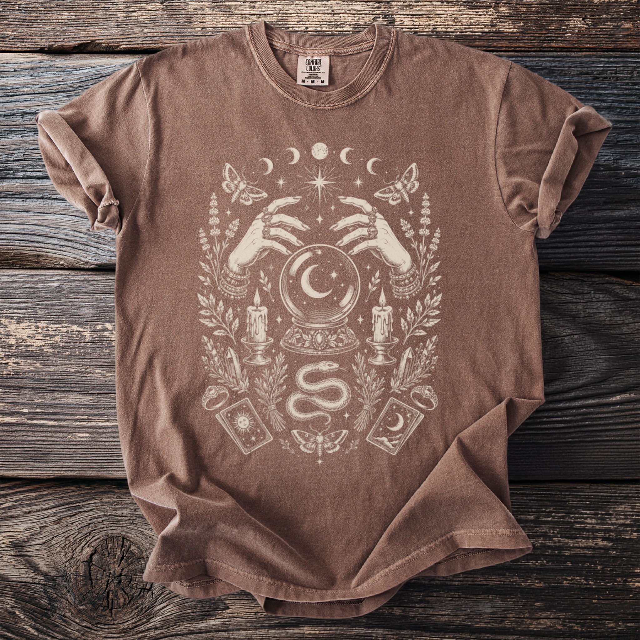 Brown t-shirt with a mystical graphic of hands, crystal ball, and celestial moon phases.