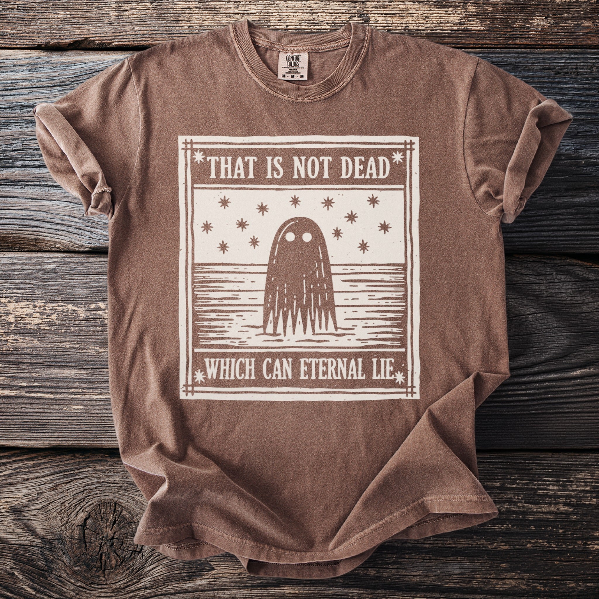 Brown t-shirt with a graphic of a ghost and text "THAT IS NOT DEAD WHICH CAN ETERNAL LIE".