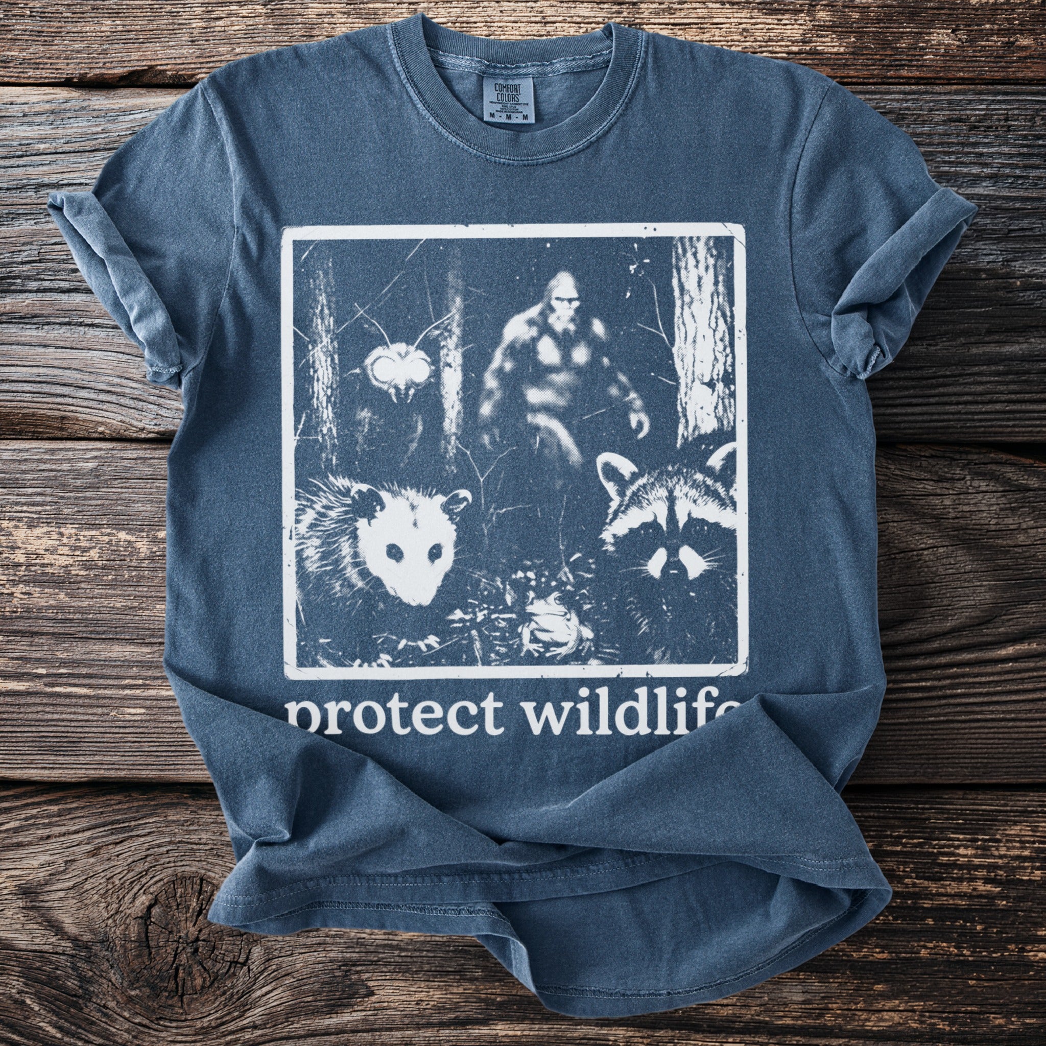 T-shirt graphic with Bigfoot, opossum, raccoon, frog, and moth, with text "protect wildlife".