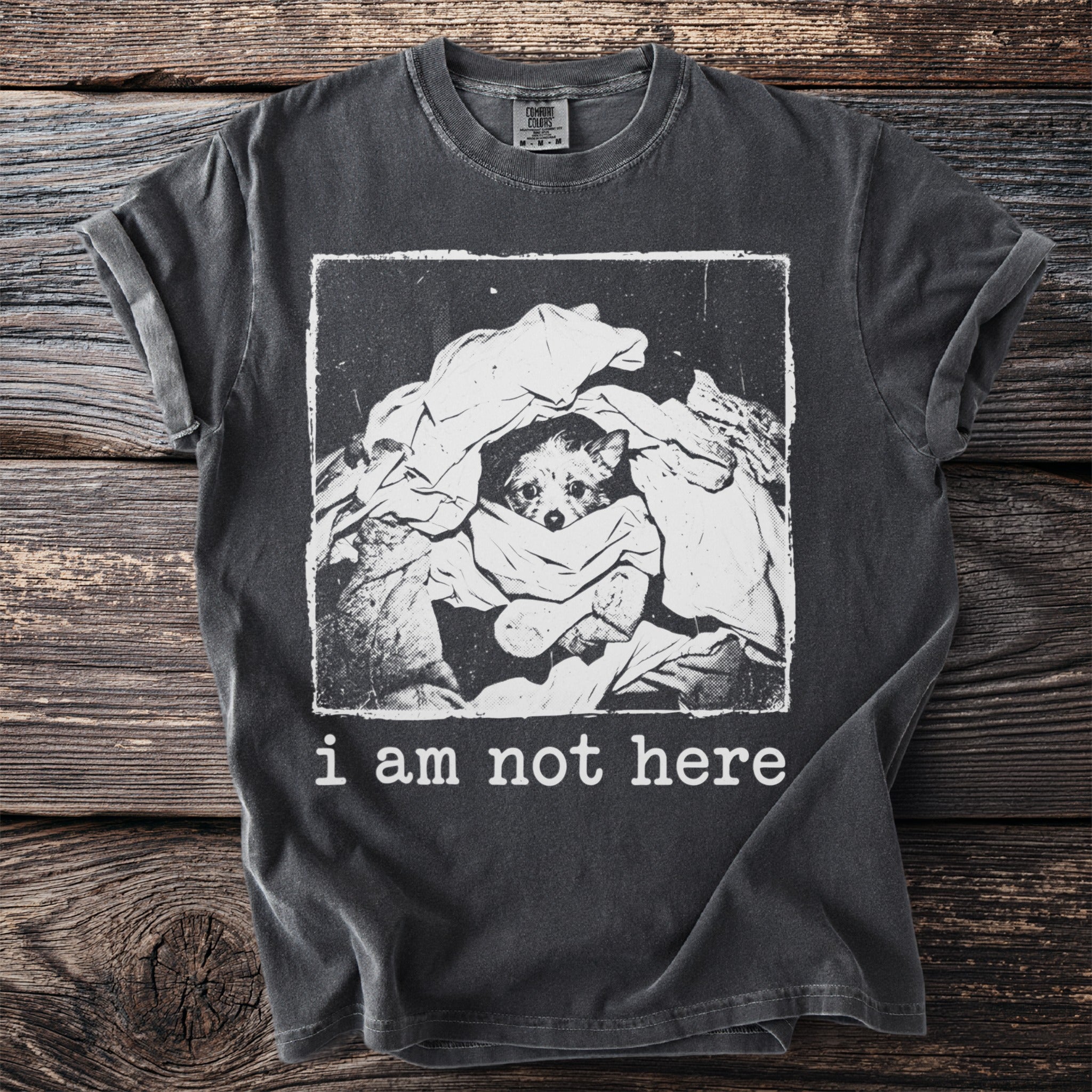 T-shirt with graphic of a dog peeking out from a pile of laundry, reading "i am not here."