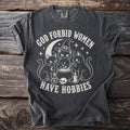 Dark gray t-shirt with "God Forbid Women Have Hobbies" text and witchy cat graphic.
