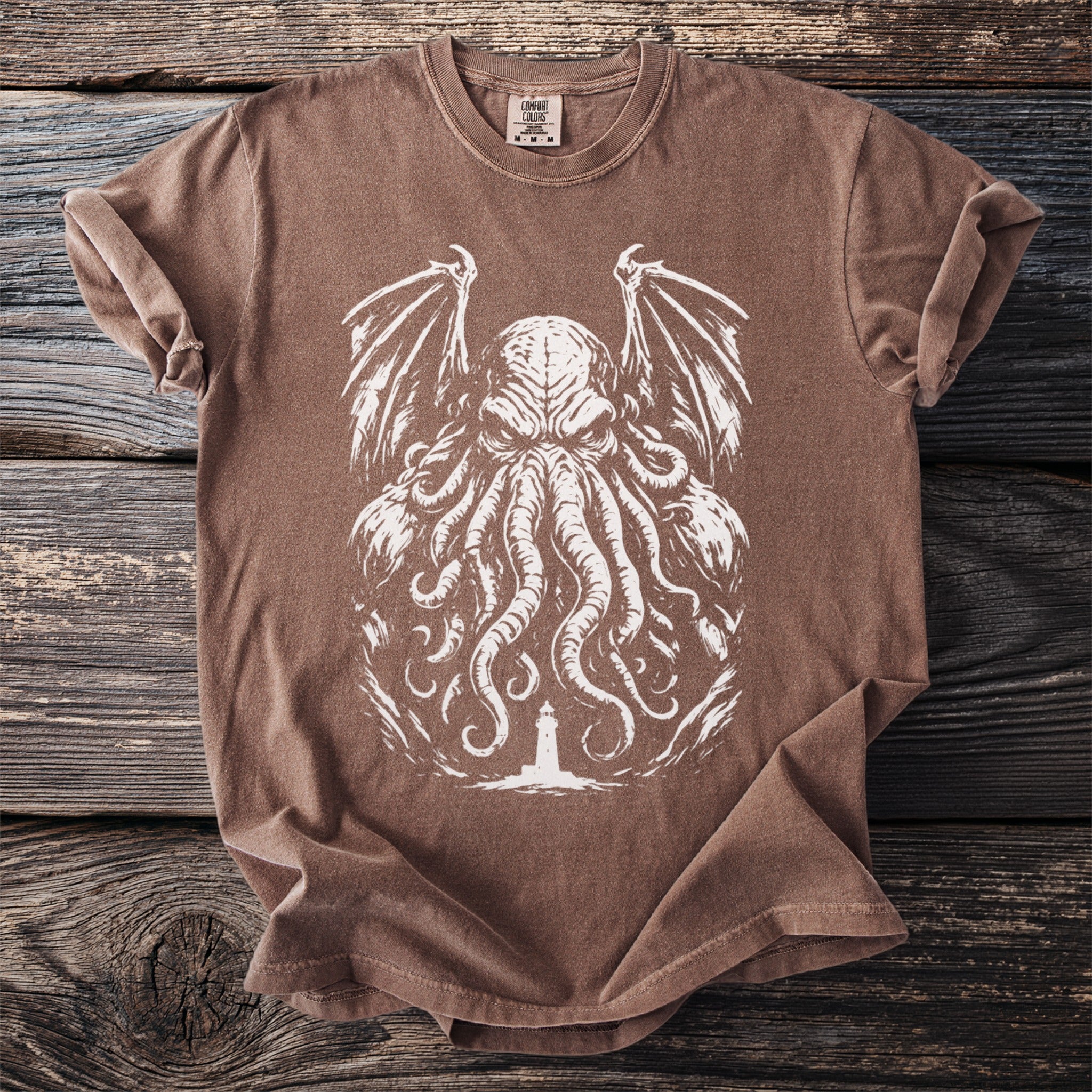 Brown t-shirt with a white graphic of a tentacled creature and a lighthouse.