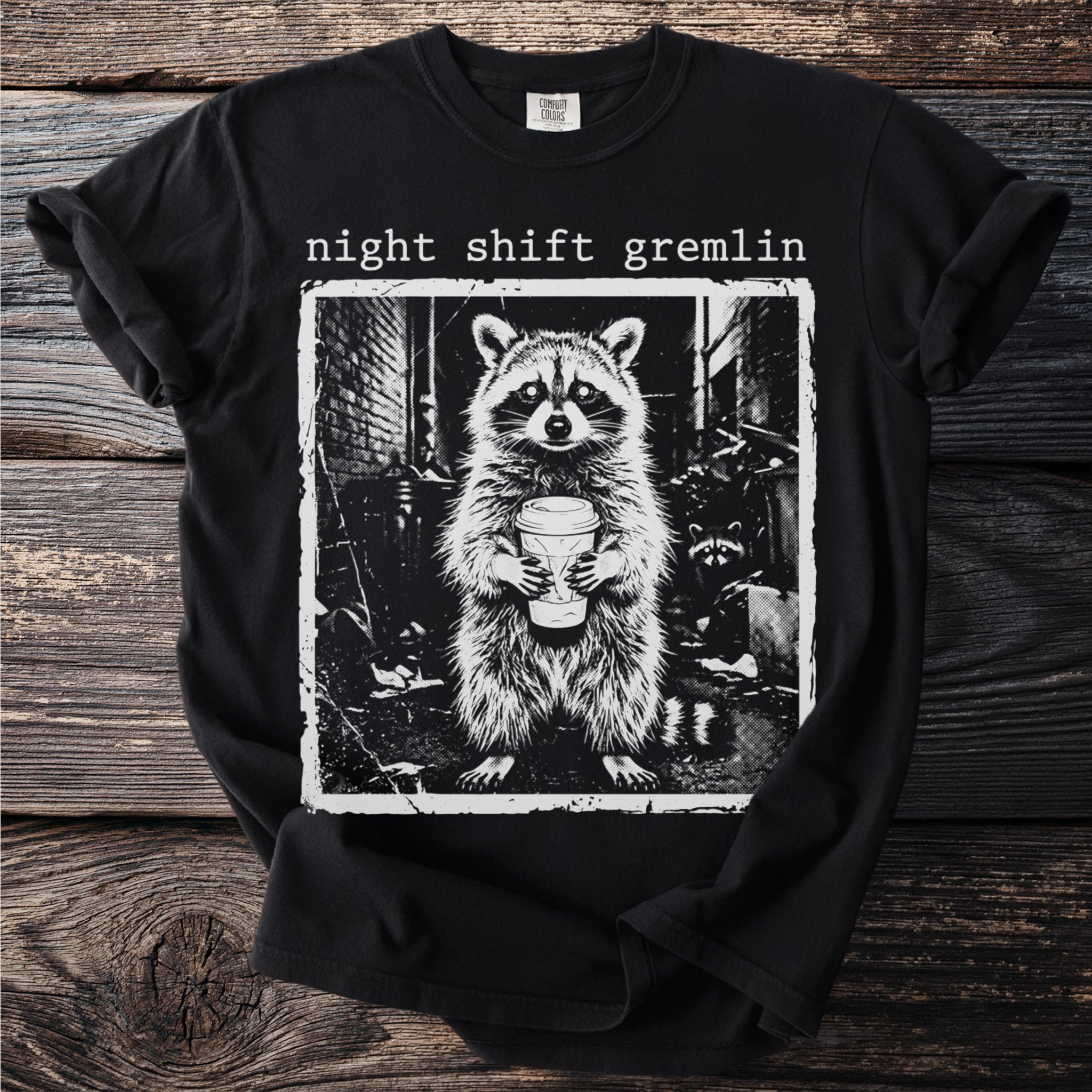 Black t-shirt with "night shift gremlin" text and raccoon holding coffee cup graphic.