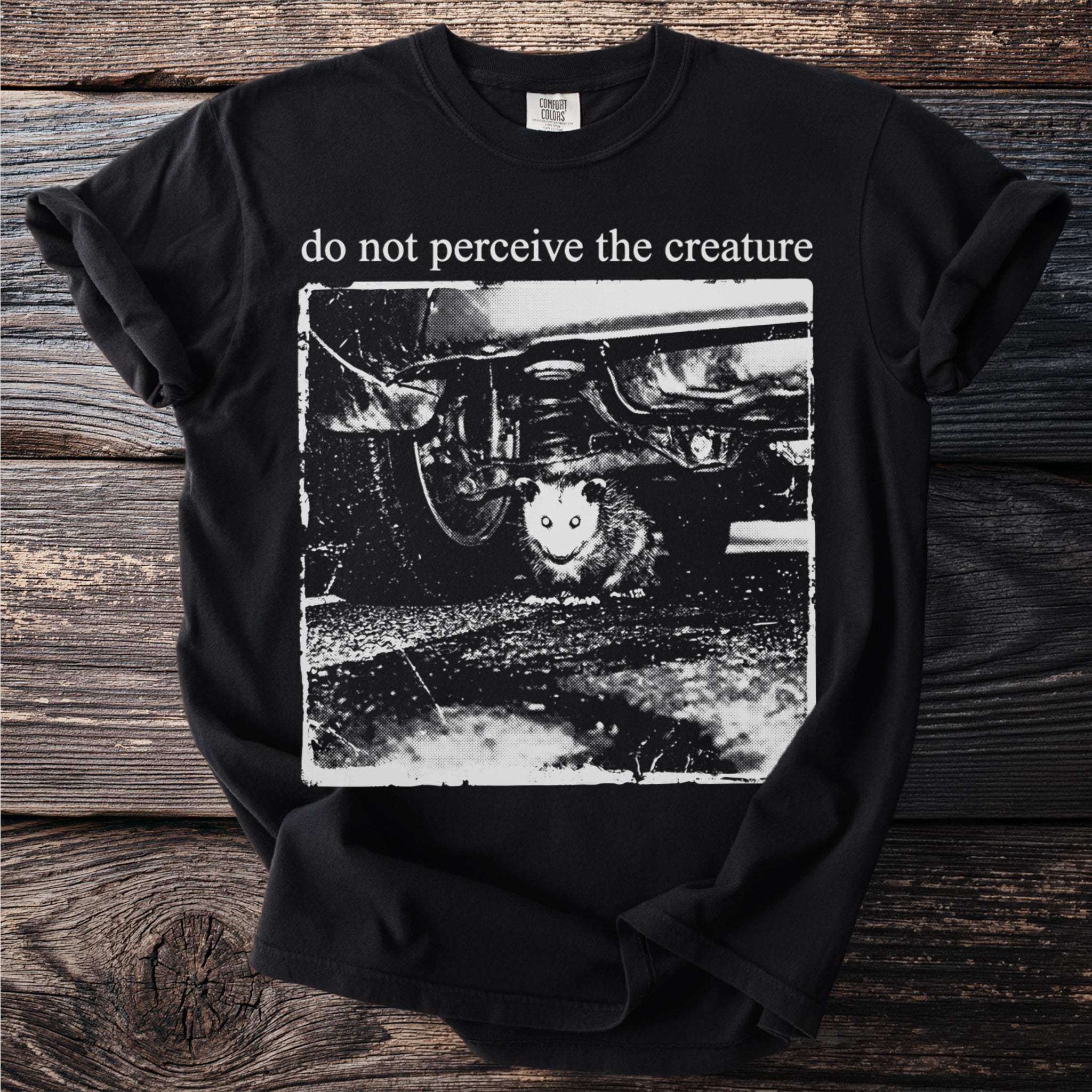 Black t-shirt with a distressed print of a possum under a car and text "do not perceive the creature".
