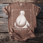 Brown t-shirt with a distressed graphic of a pelican and the text "holding it all in".
