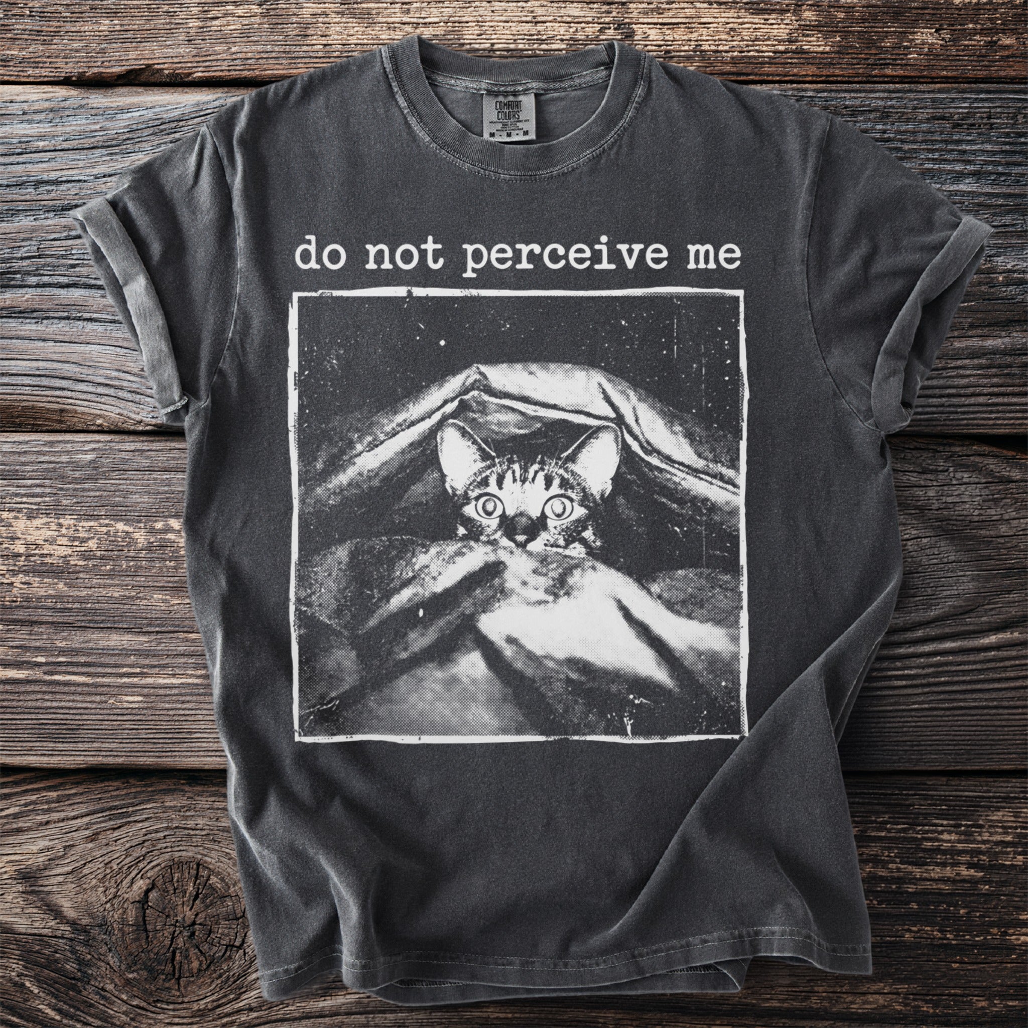 Dark gray t-shirt with a distressed print of a shy cat peeking from under a blanket and the text "do not perceive me".