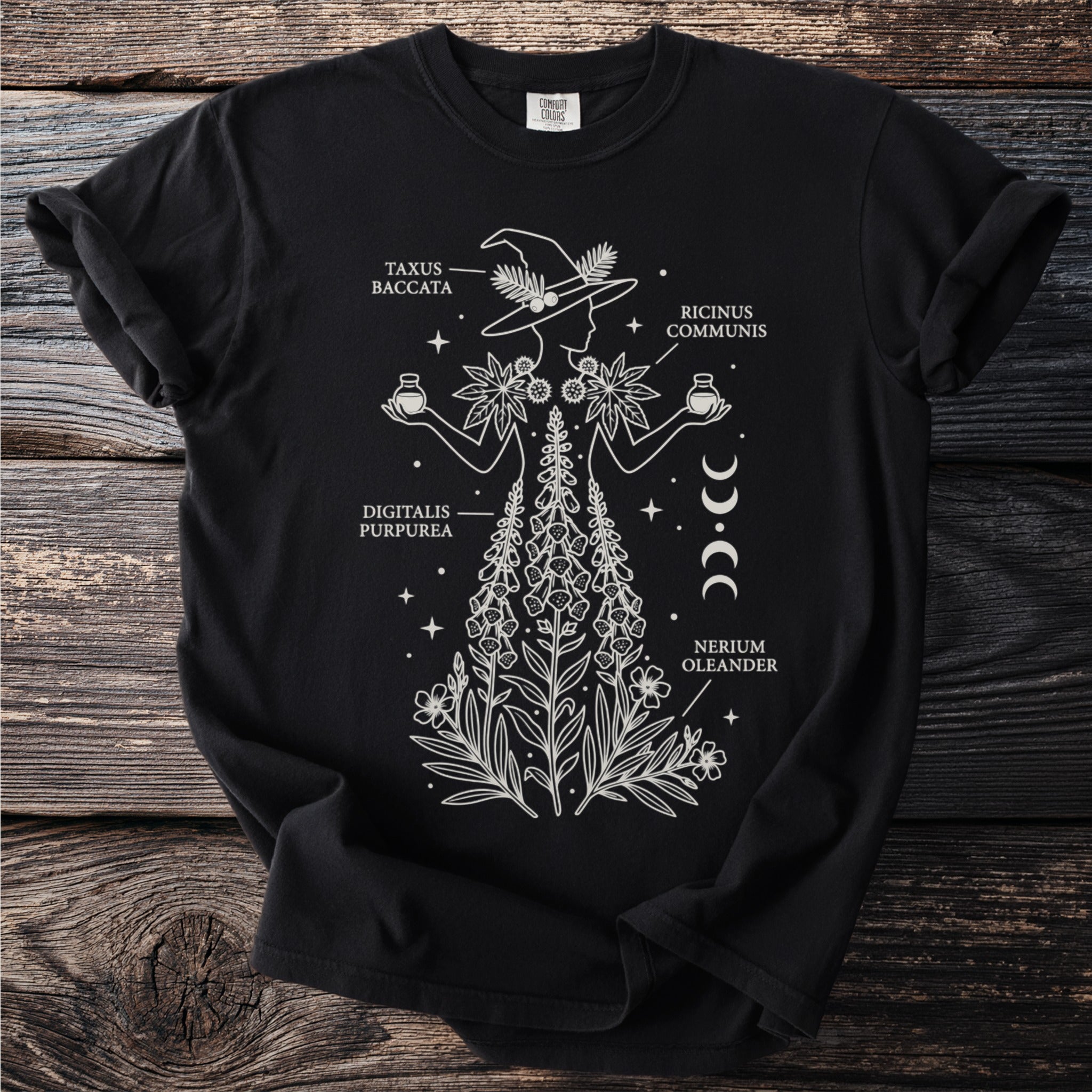 Black t-shirt with white line art of a witch and botanical illustrations with labels: Taxus Baccata, Digitalis Purpurea, Ricinus Communis, Nerium Oleander.