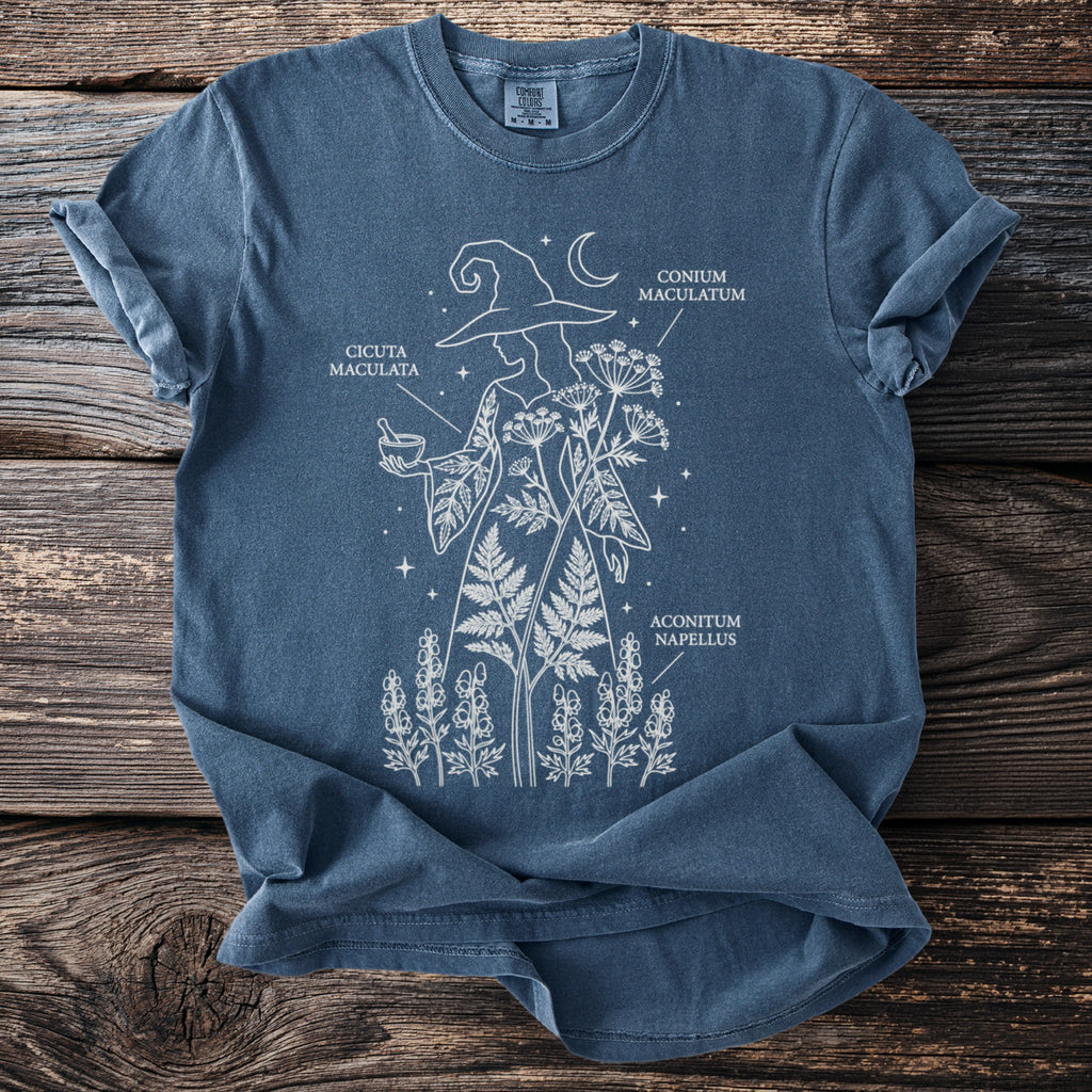 Blue t-shirt with white line art of a witch holding potion, plants labeled "Cicuta Maculata," "Conium Maculatum," and "Aconitum Napellus."