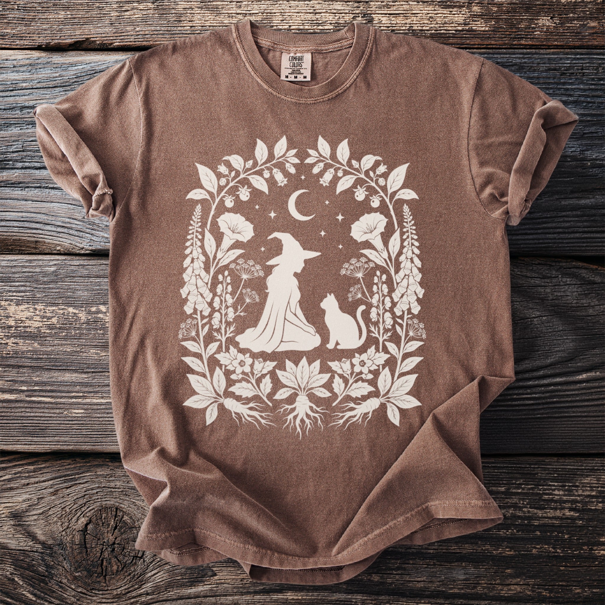 Brown t-shirt with white witch, cat, moon, and floral design.