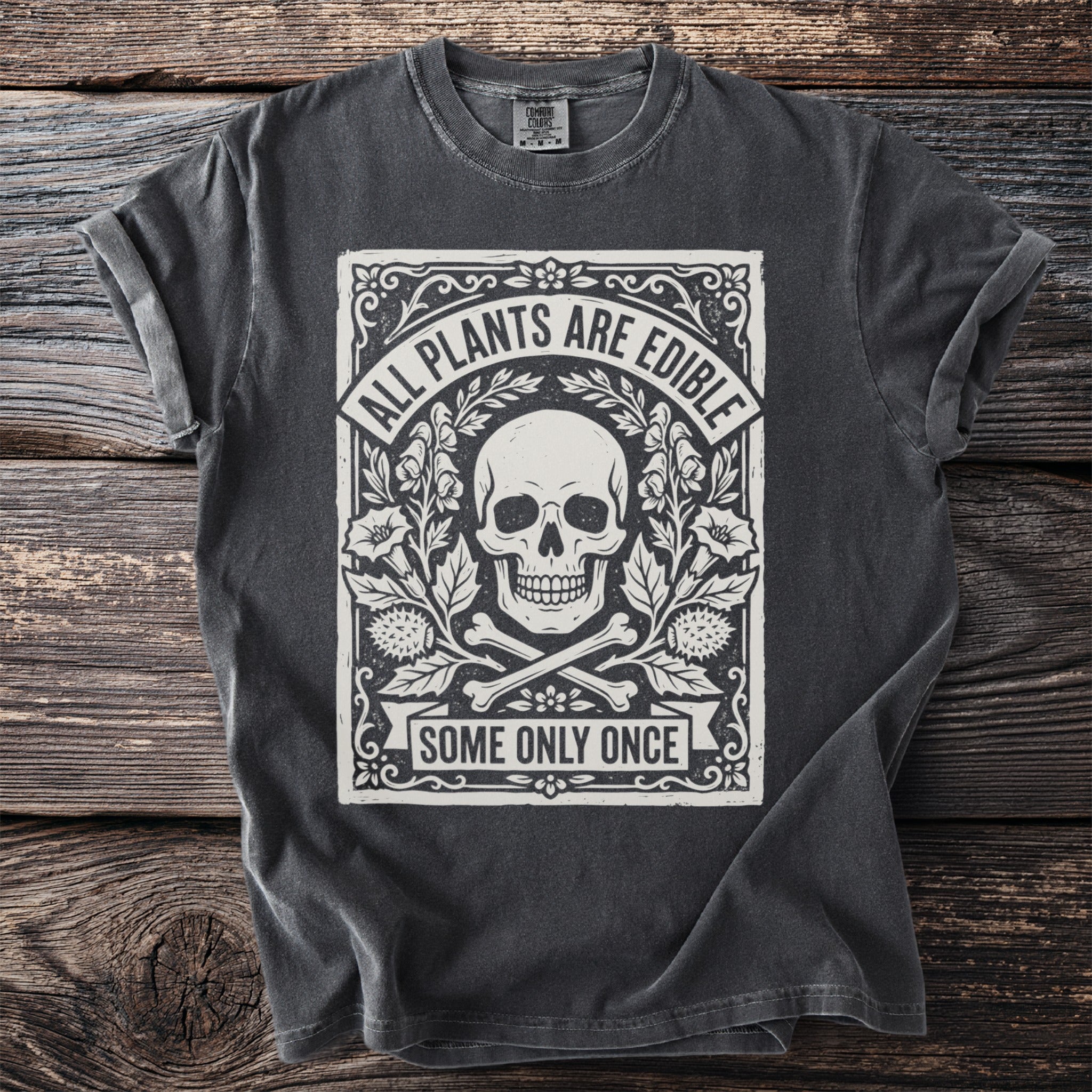 Dark grey t-shirt with a skull, bones, plants, and text "ALL PLANTS ARE EDIBLE SOME ONLY ONCE".