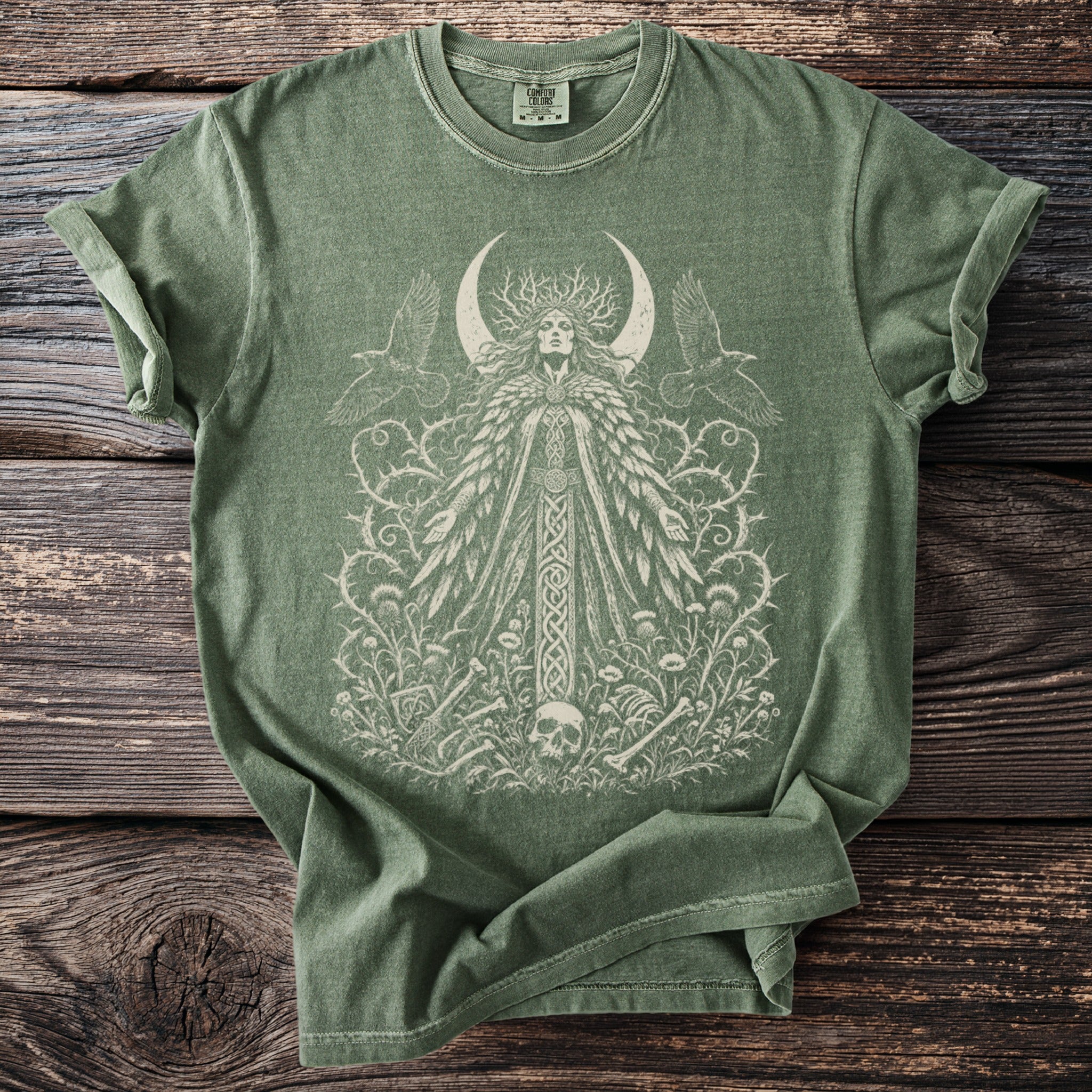 Green t-shirt with a central print of a female figure with a crescent moon and ravens.