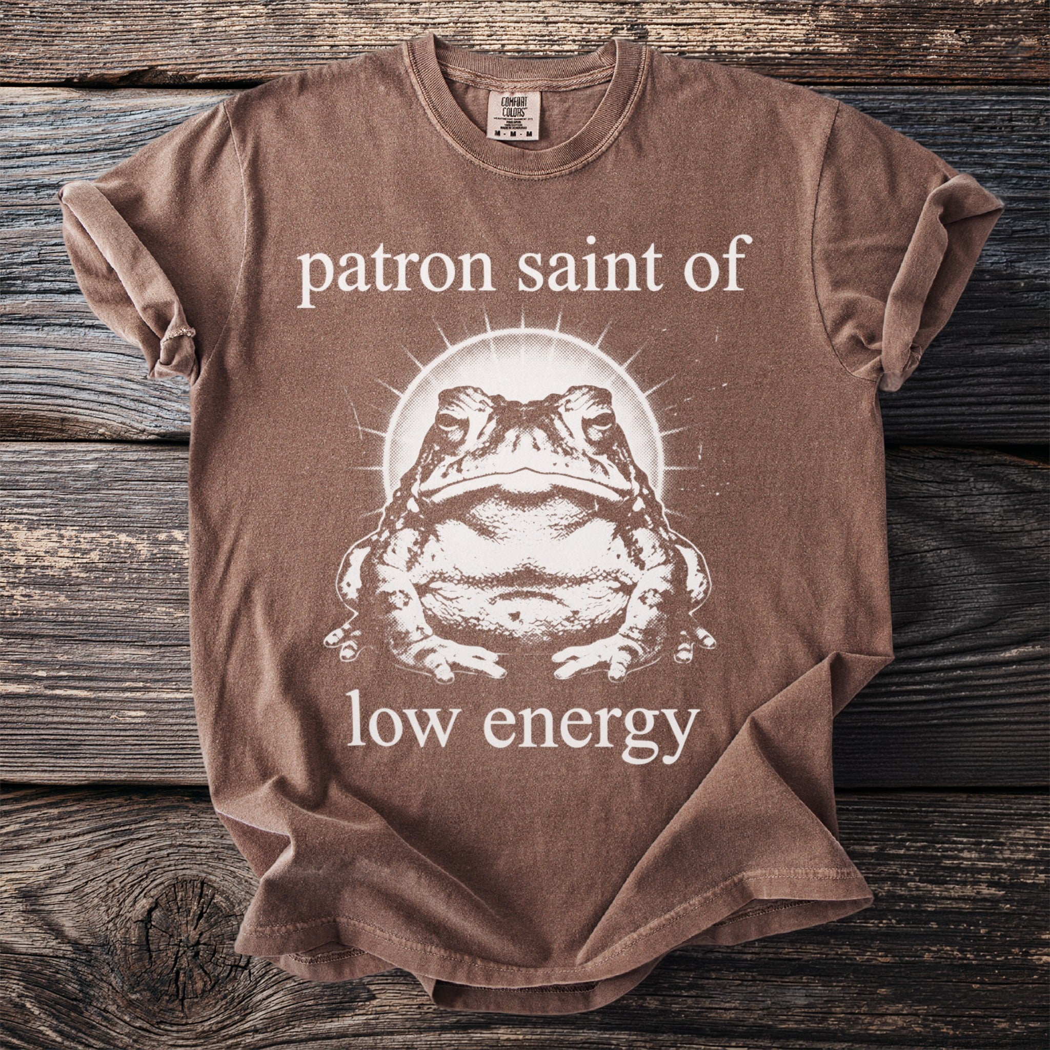 Brown t-shirt with a toad graphic and text reading "patron saint of low energy".