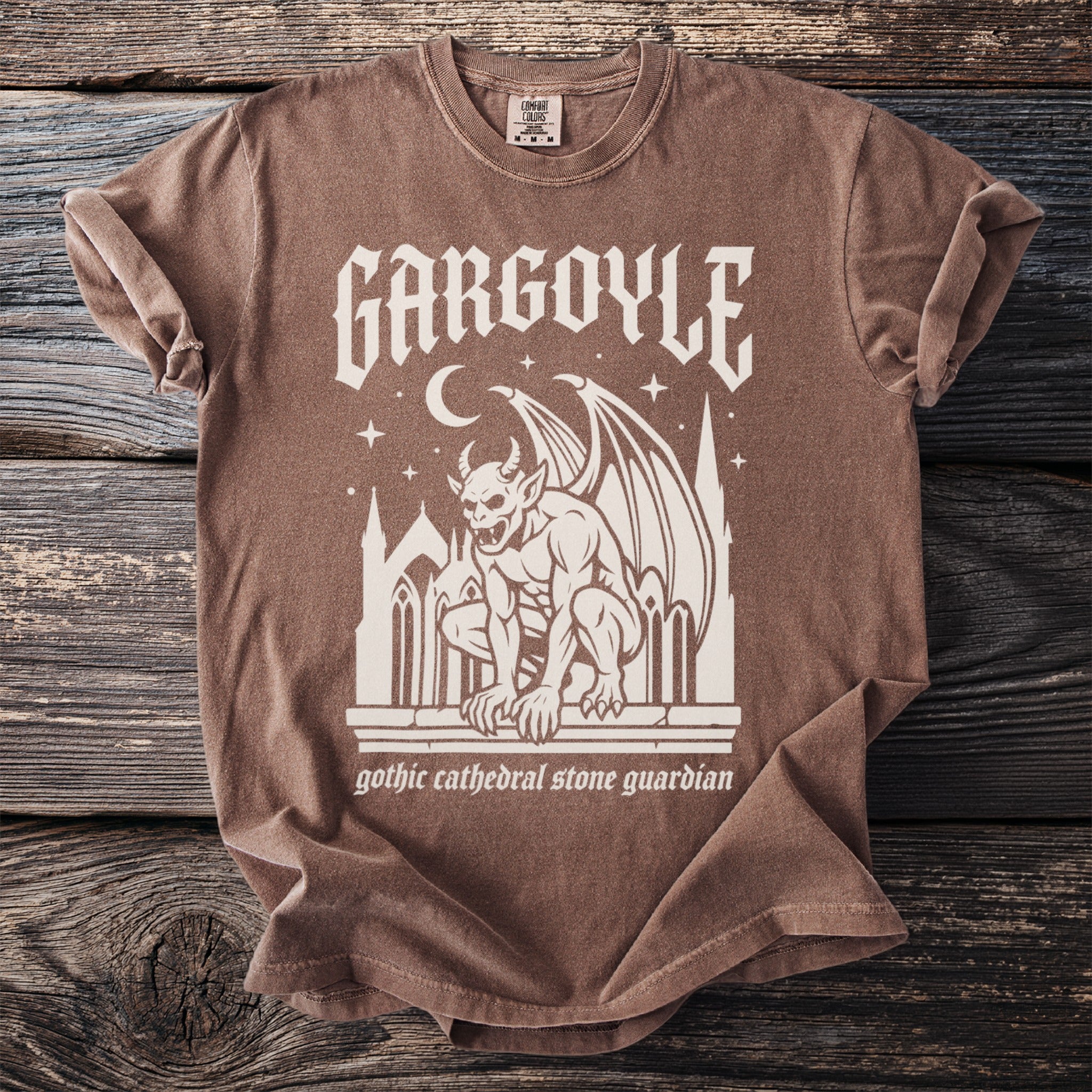 Brown t-shirt with cream gothic graphic featuring a winged gargoyle and text.