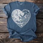 Blue t-shirt with white linework art of two cats forming a heart with floral accents and a moon.