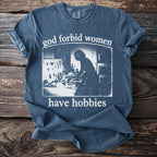 Blue t-shirt with distressed text "god forbid women have hobbies" and silhouetted image.