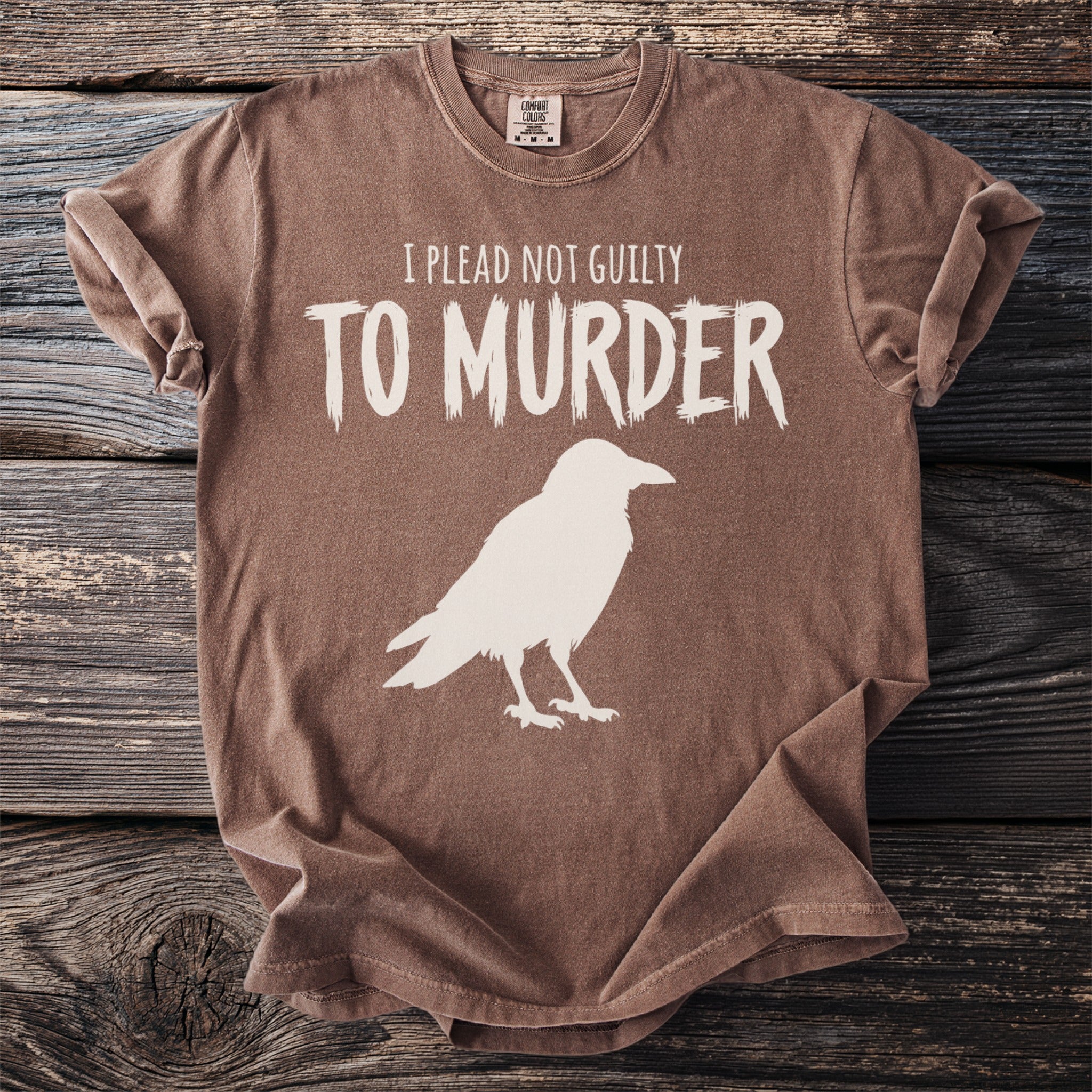 Brown t-shirt with white text "I PLEAD NOT GUILTY TO MURDER" and crow silhouette.