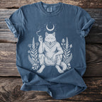 Blue t-shirt with white illustration of a wolfman smoking, surrounded by plants and a crescent moon.