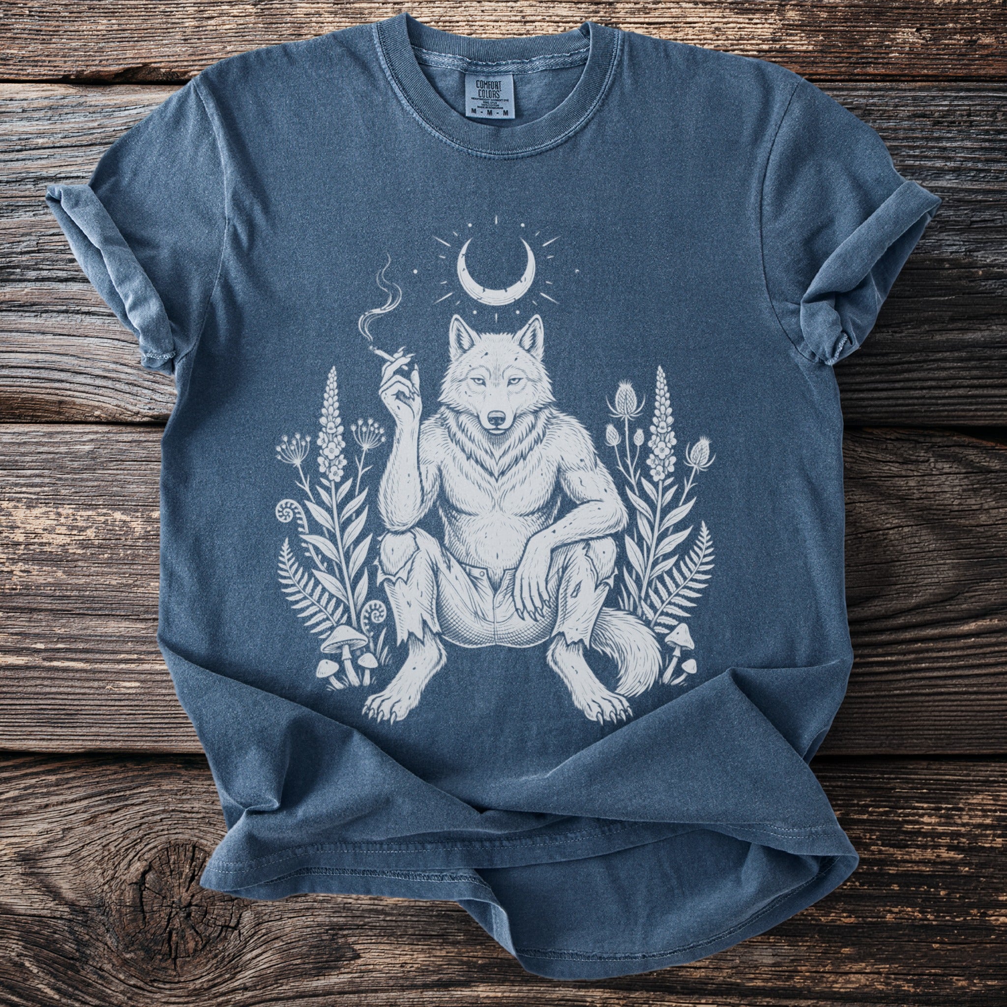 Blue t-shirt with white illustration of a wolfman smoking, surrounded by plants and a crescent moon.