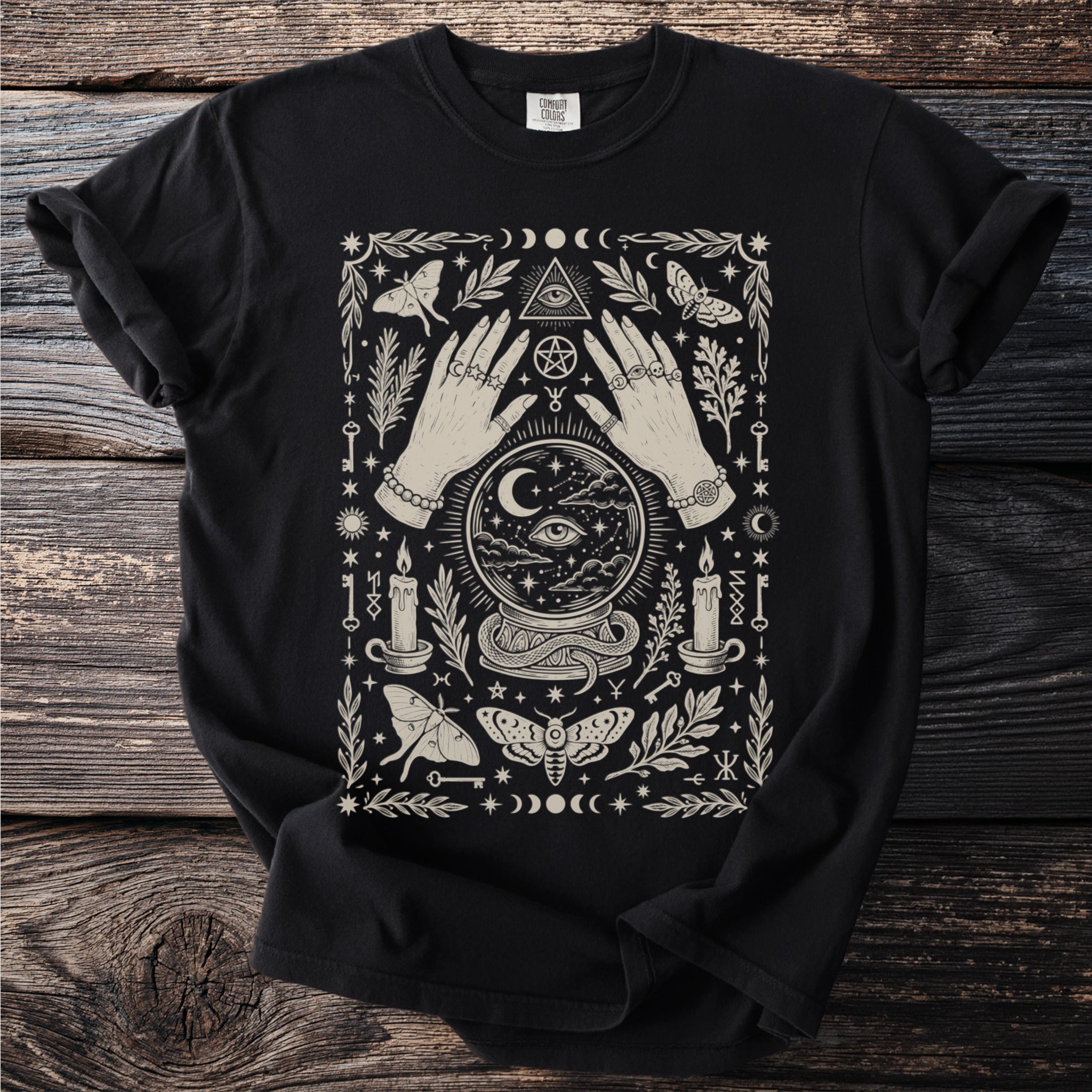 Black t-shirt with cream graphic featuring hands, crystal ball, moths, candles, and celestial symbols.