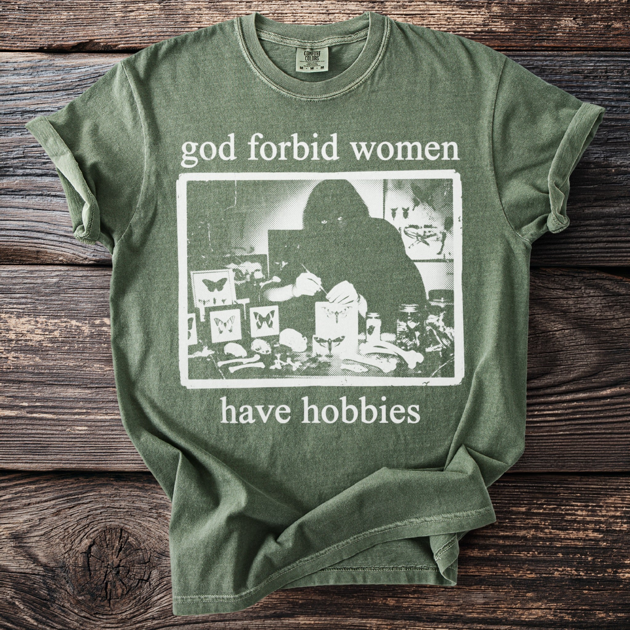Green t-shirt with "god forbid women have hobbies" and a graphic of a person collecting insects.