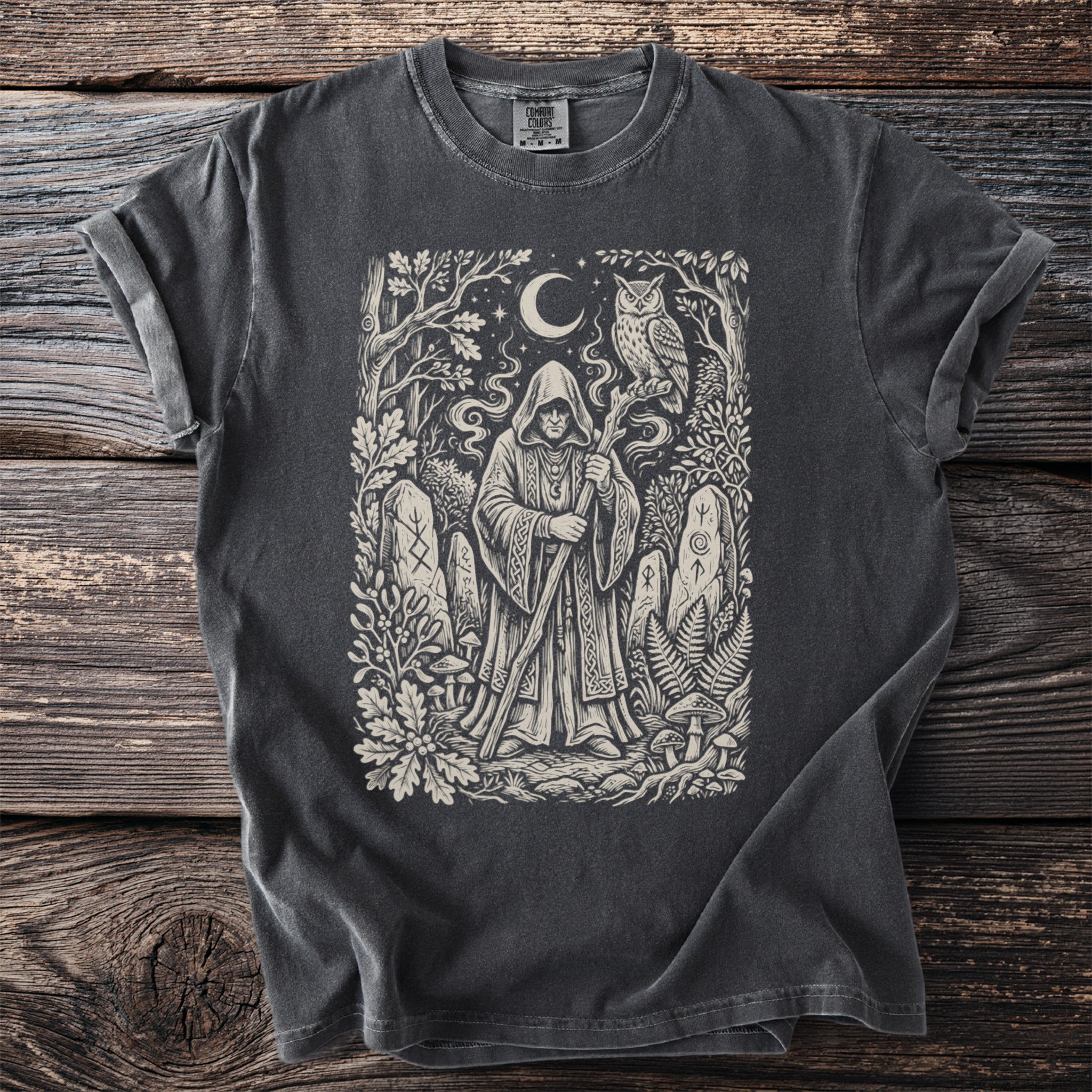 Dark t-shirt with a graphic of a hooded figure, owl, moon, and runes in a forest.