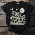 Black t-shirt with a beige graphic of bats, moon, flowers, grass, and a fence.