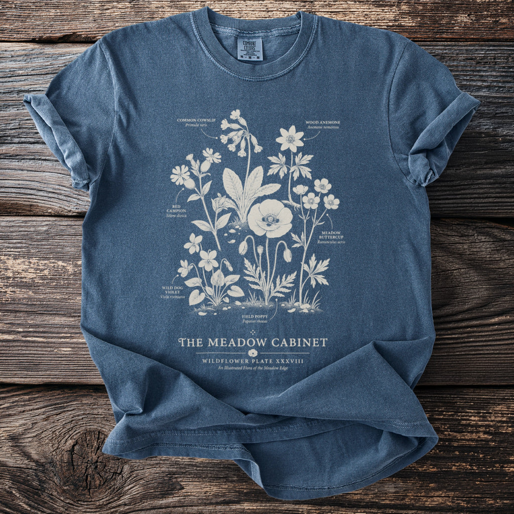 Blue t-shirt with botanical illustration of wildflowers and text "The Meadow Cabinet".