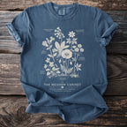 Blue t-shirt with botanical illustration of wildflowers and text "The Meadow Cabinet".
