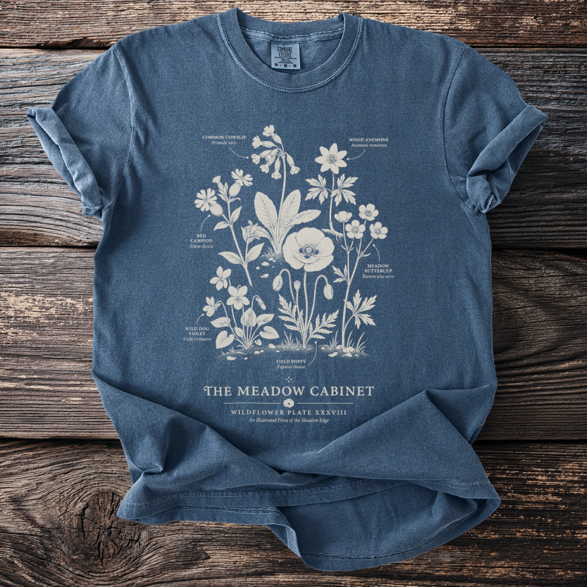 Blue t-shirt with botanical illustration of wildflowers and text "The Meadow Cabinet".
