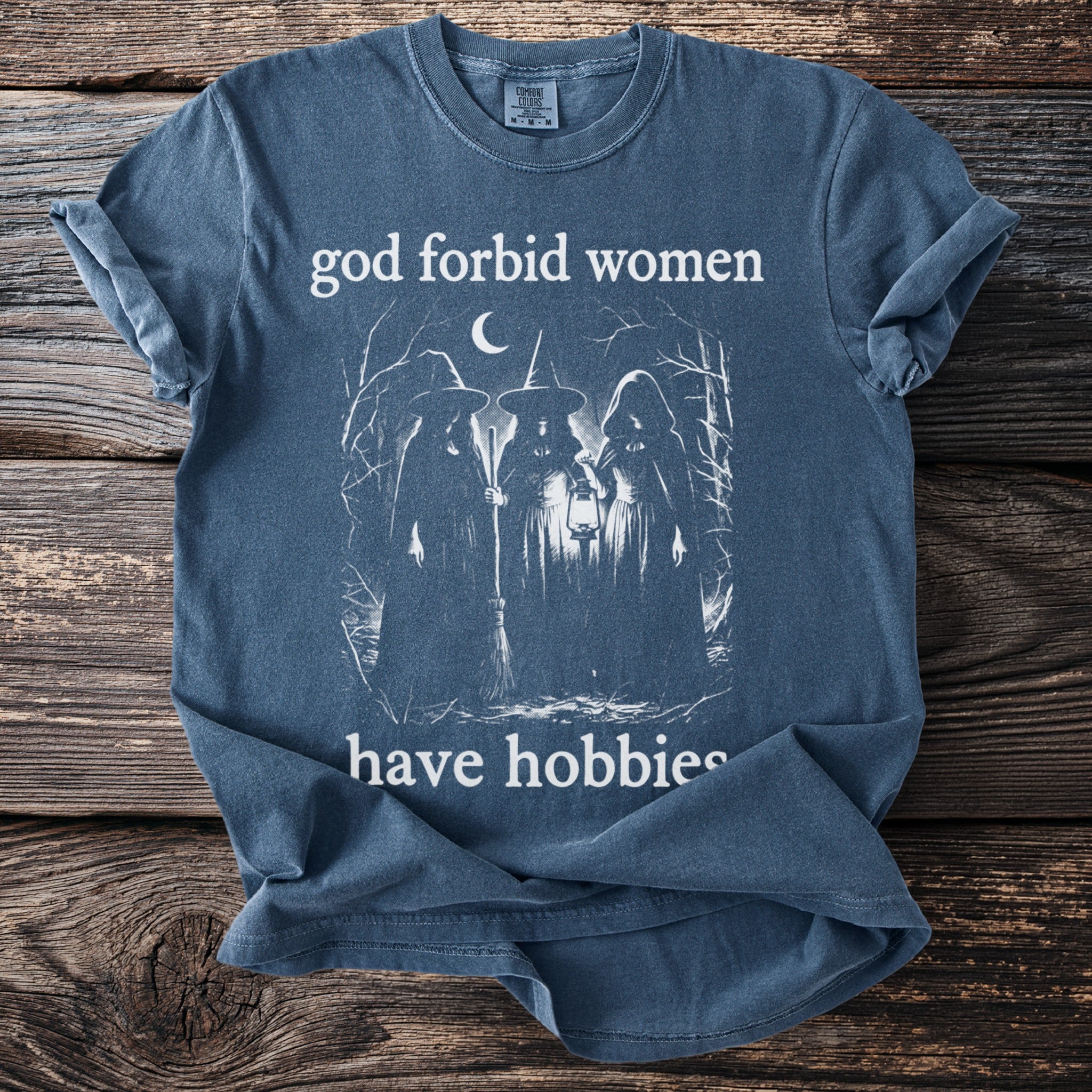Blue t-shirt with white graphic of three witches and text "god forbid women have hobbies".