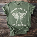 Green t-shirt with white text and moth graphic saying "God forbid women have hobbies."