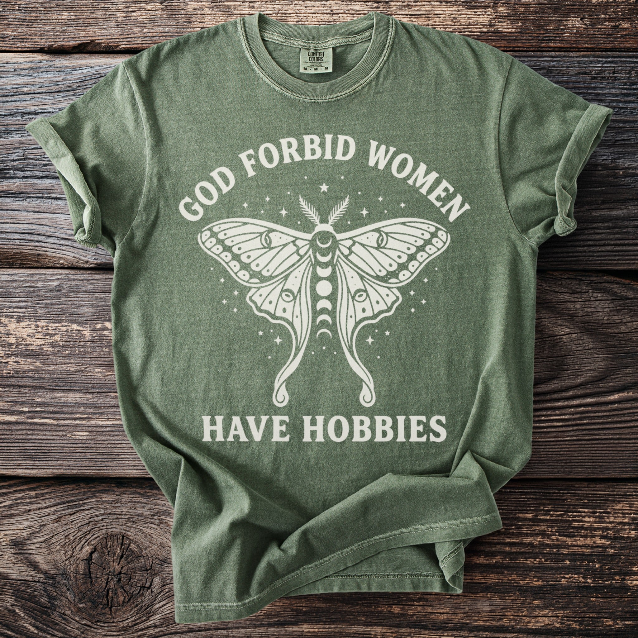 Green t-shirt with white text and moth graphic saying "God forbid women have hobbies."