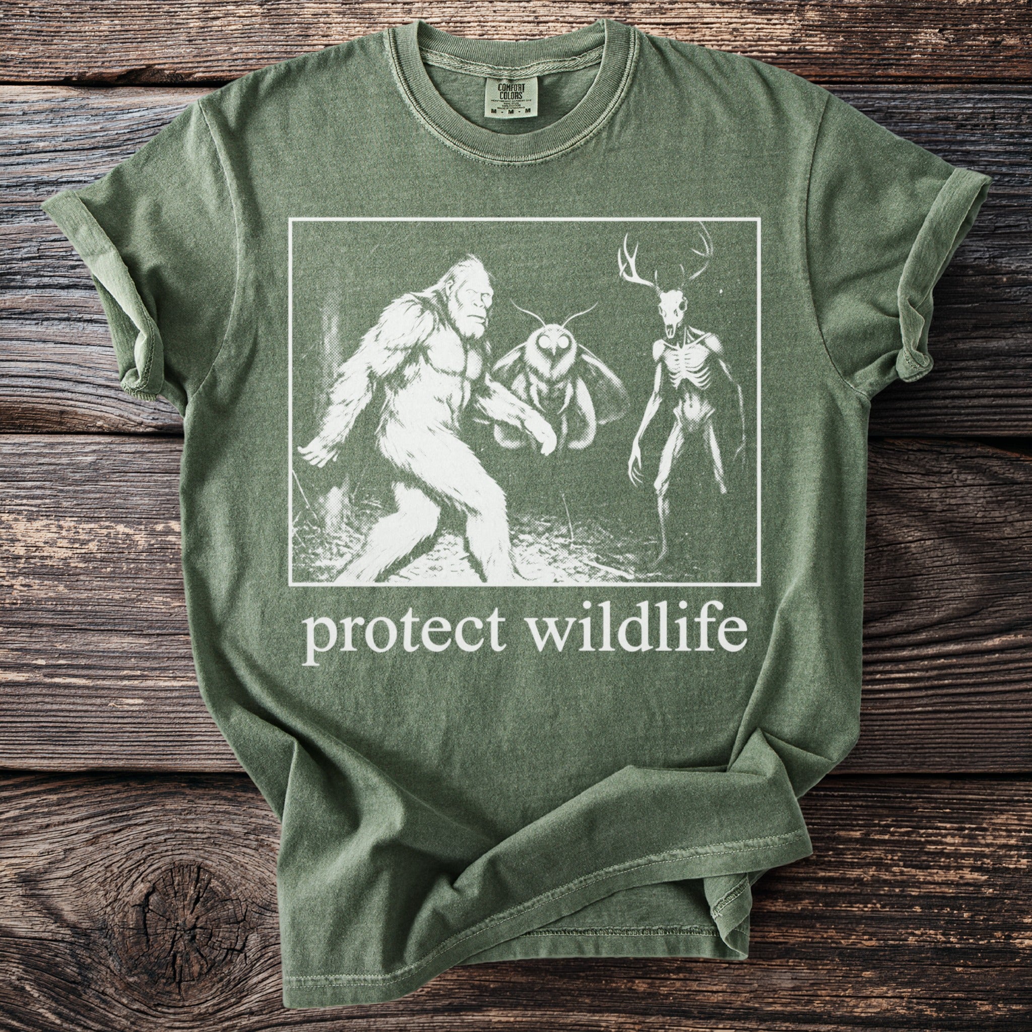 Green t-shirt with Bigfoot, moth, and skeleton deer graphic and "protect wildlife" text.