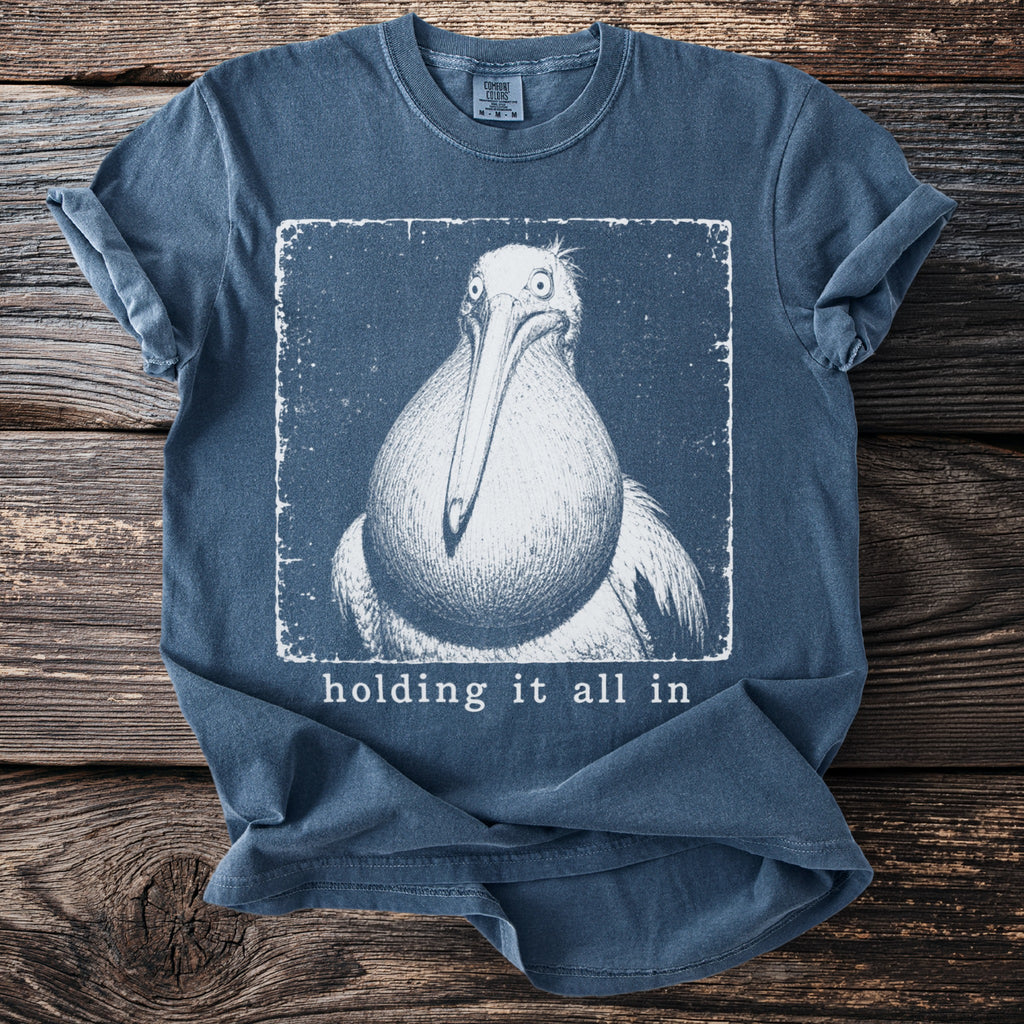 Blue t-shirt with a vintage-style drawing of a pelican and the text "holding it all in".