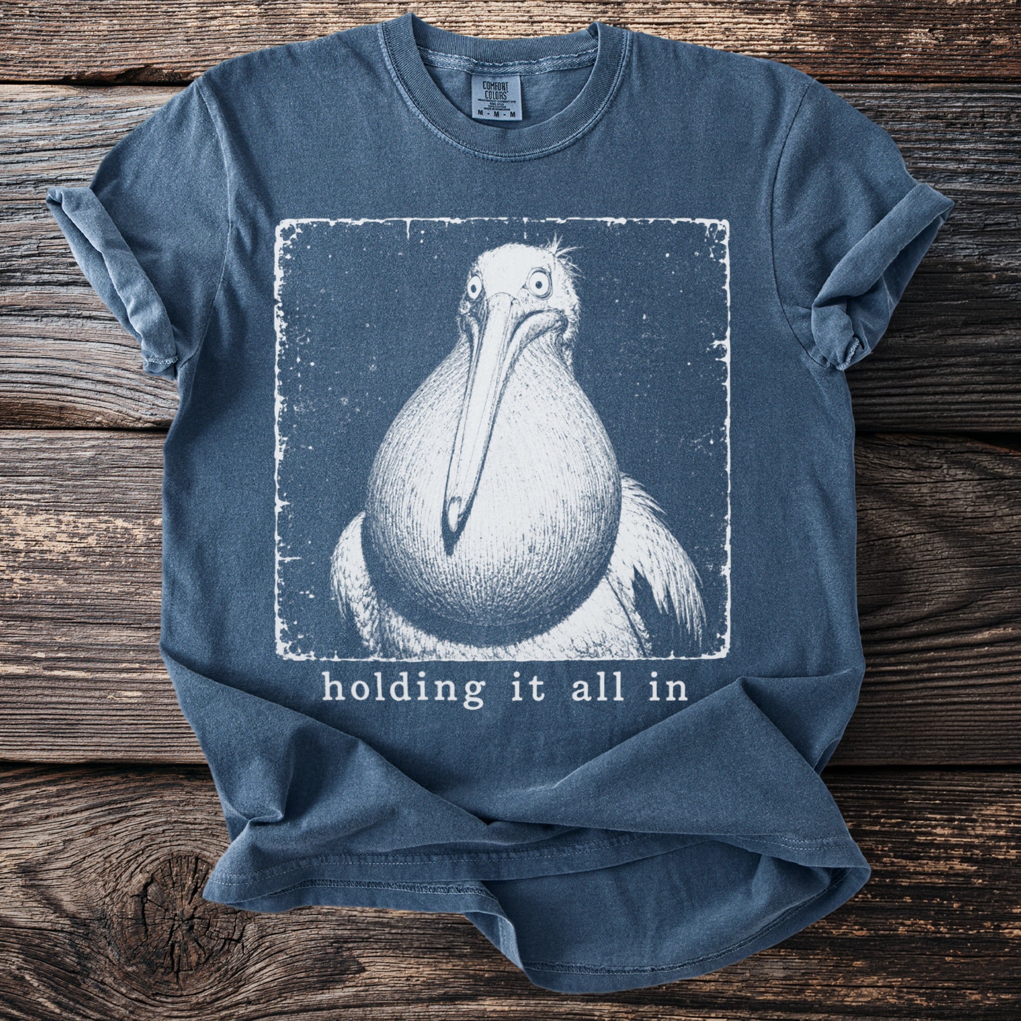 Blue t-shirt with a vintage-style drawing of a pelican and the text "holding it all in".