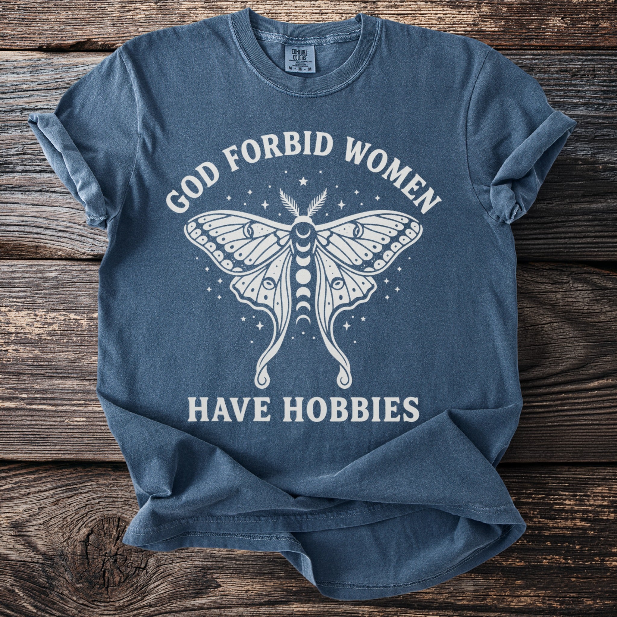 Blue t-shirt with white text "GOD FORBID WOMEN HAVE HOBBIES" and a moth graphic.