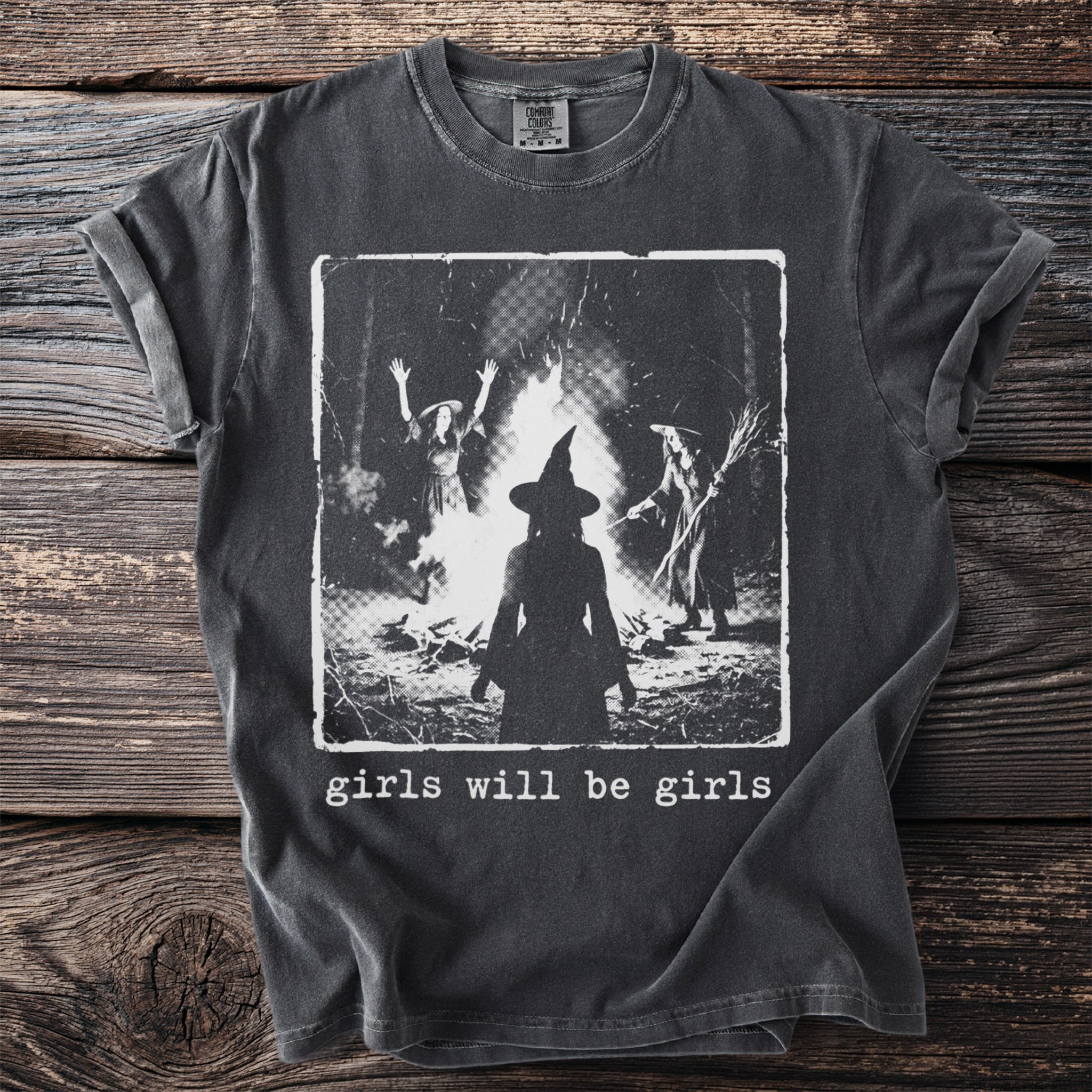 Dark grey t-shirt with image of witches around a campfire and text "girls will be girls".