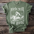 Green t-shirt with white graphic of mermaid pulling person into water and text "girls will be girls".