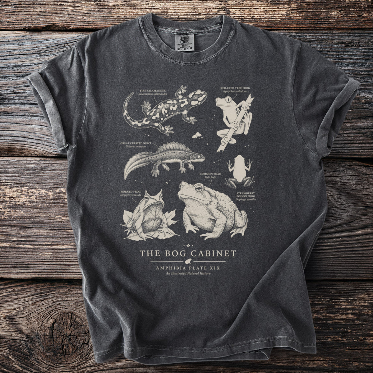 Dark grey t-shirt featuring "The Bog Cabinet" text and detailed illustrations of amphibians and a salamander.