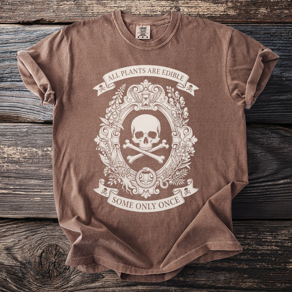 Brown t-shirt with a cream oval graphic of a skull and crossbones, botanical elements, and text.