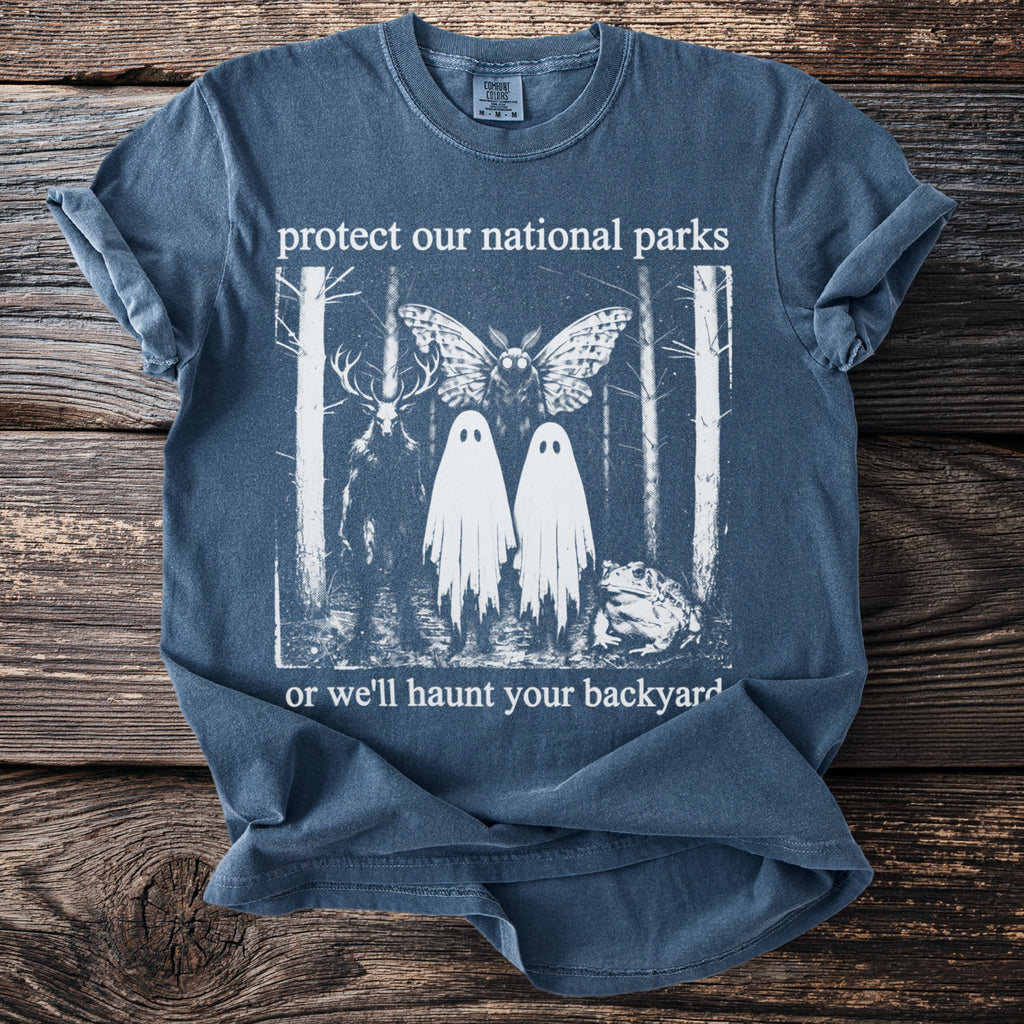 T-shirt with deer, moth, two ghosts, and frog in a forest, reading "protect our national parks or we'll haunt your backyard."