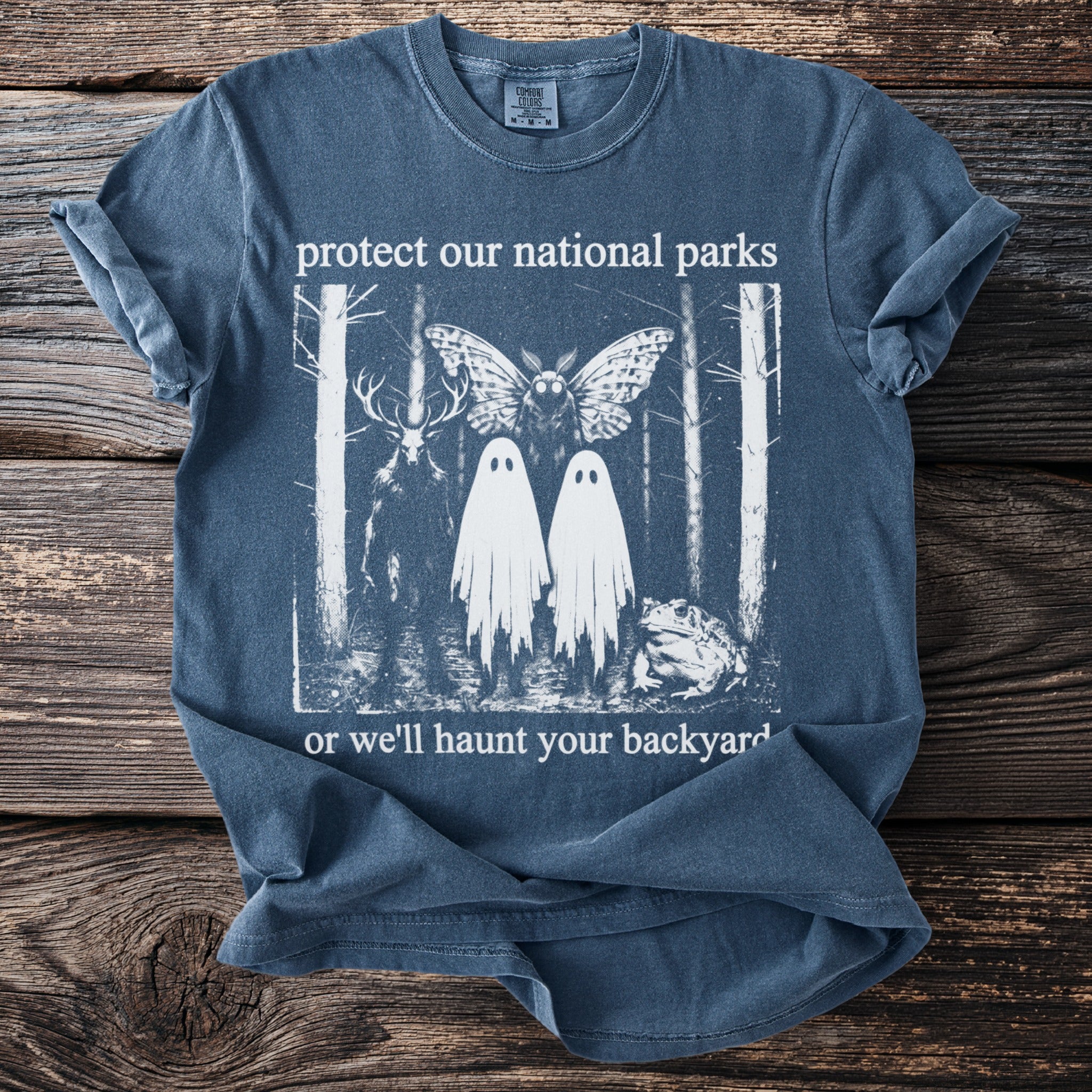 T-shirt with deer, moth, two ghosts, and frog in a forest, reading "protect our national parks or we'll haunt your backyard."