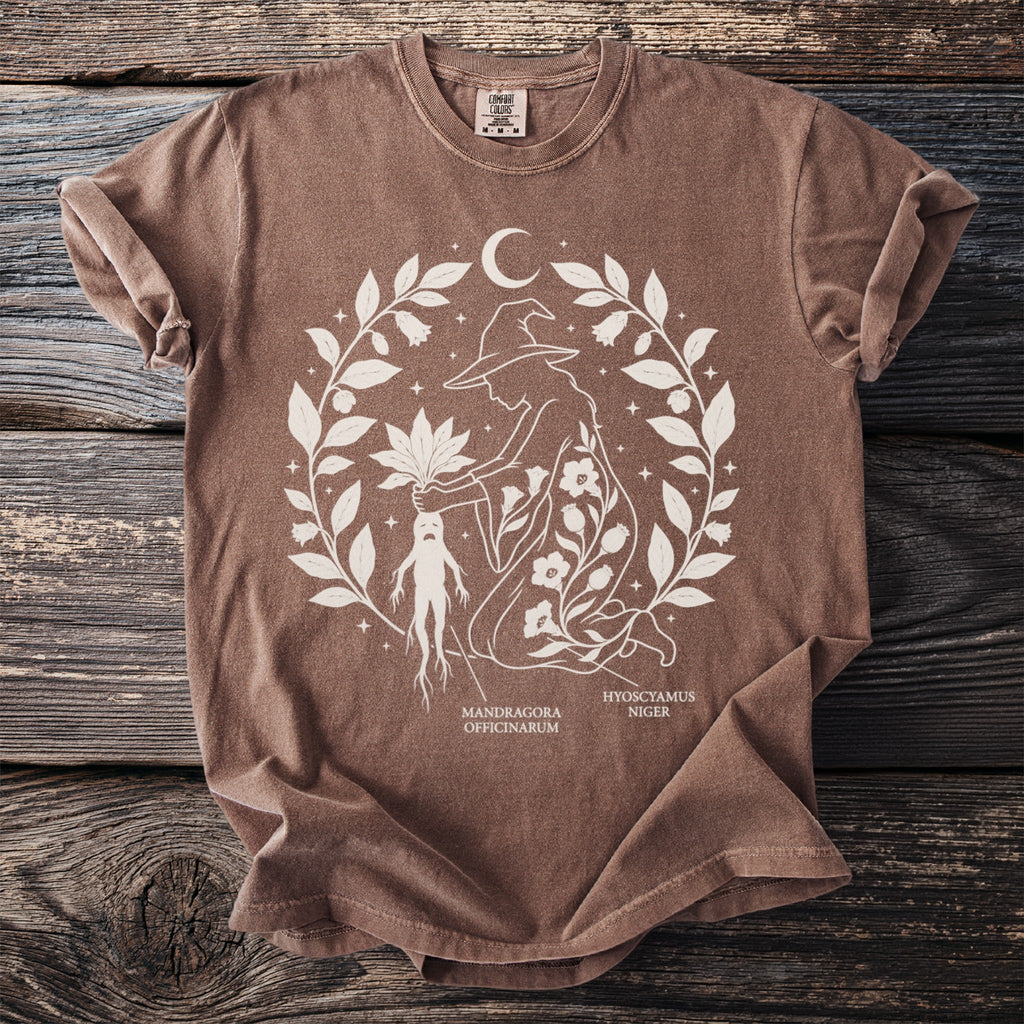 Brown t-shirt with botanical illustration featuring a witch, mandrake, and moon.